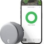 August Home Smart Lock in a sleek, silver cylindrical design, installed on a front door, showcasing its keyless entry system. The smart lock emphasizes remote access via smartphone, with compatibility for Alexa, Google Assistant, and Apple HomeKit, offering enhanced security and convenience for smart home users.