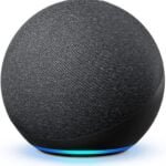 Amazon Echo (4th Gen) smart speaker in a spherical design with a charcoal finish, placed on a contemporary living room shelf. The device features a glowing blue LED ring at the base, indicating Alexa is active. It offers 360-degree audio and smart home integration through voice control.