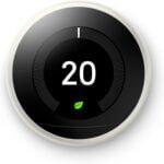 Google Nest Thermostat with a sleek circular design in a frosted white finish, mounted on a modern living room wall. The digital display shows the current room temperature and energy-saving settings, emphasizing its smart control features for optimizing home heating and cooling.